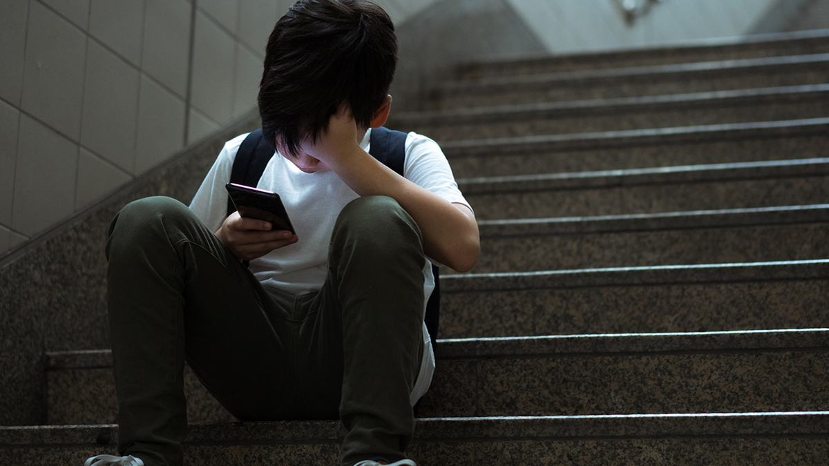 Little boy looking discouraged at phone on school steps