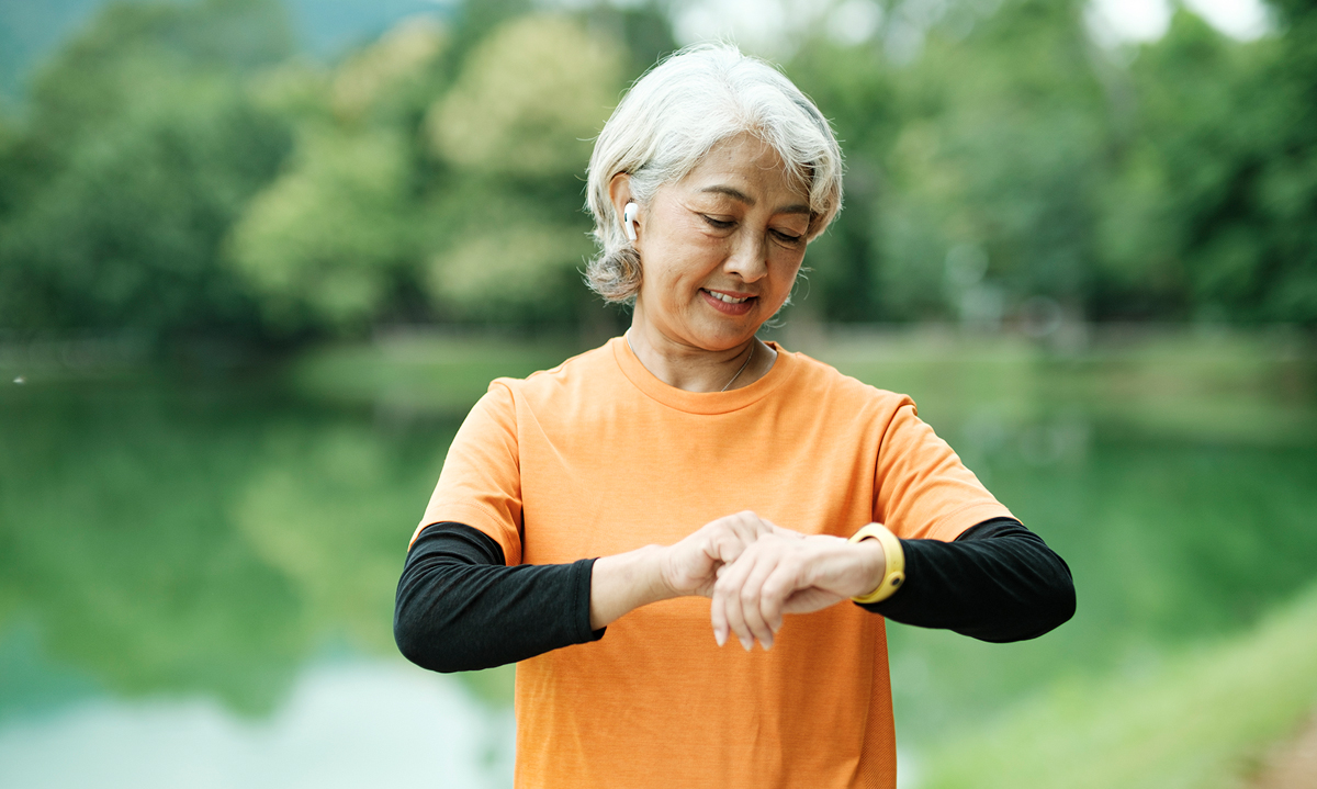 Senior woman looking at smart watch on her run through the park