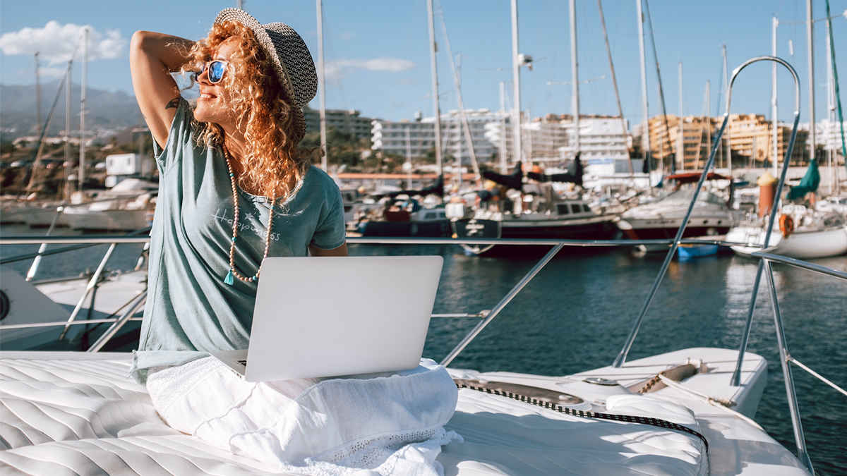Woman on laptop on sailboat in harbor