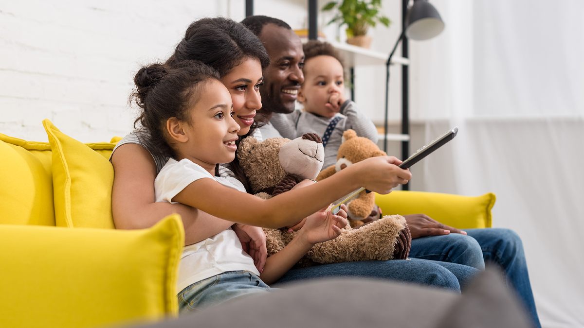 Young family watching TV together on bright yellow couch