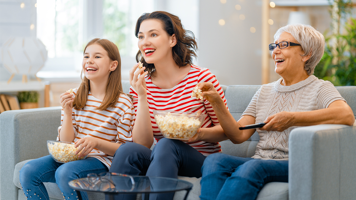 Mother, daughter, and grandmother, watching TV and eating popcorn together