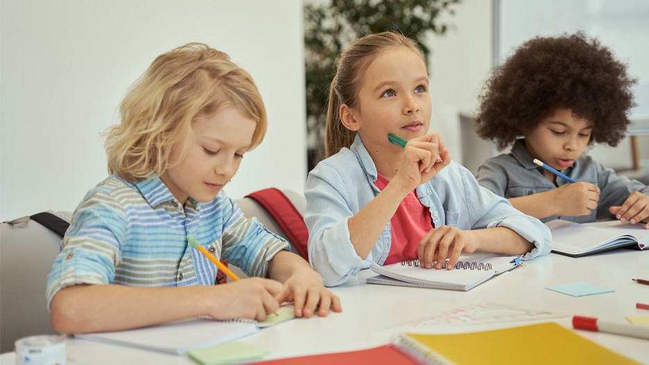 Kids in class thinking and writing in notebooks