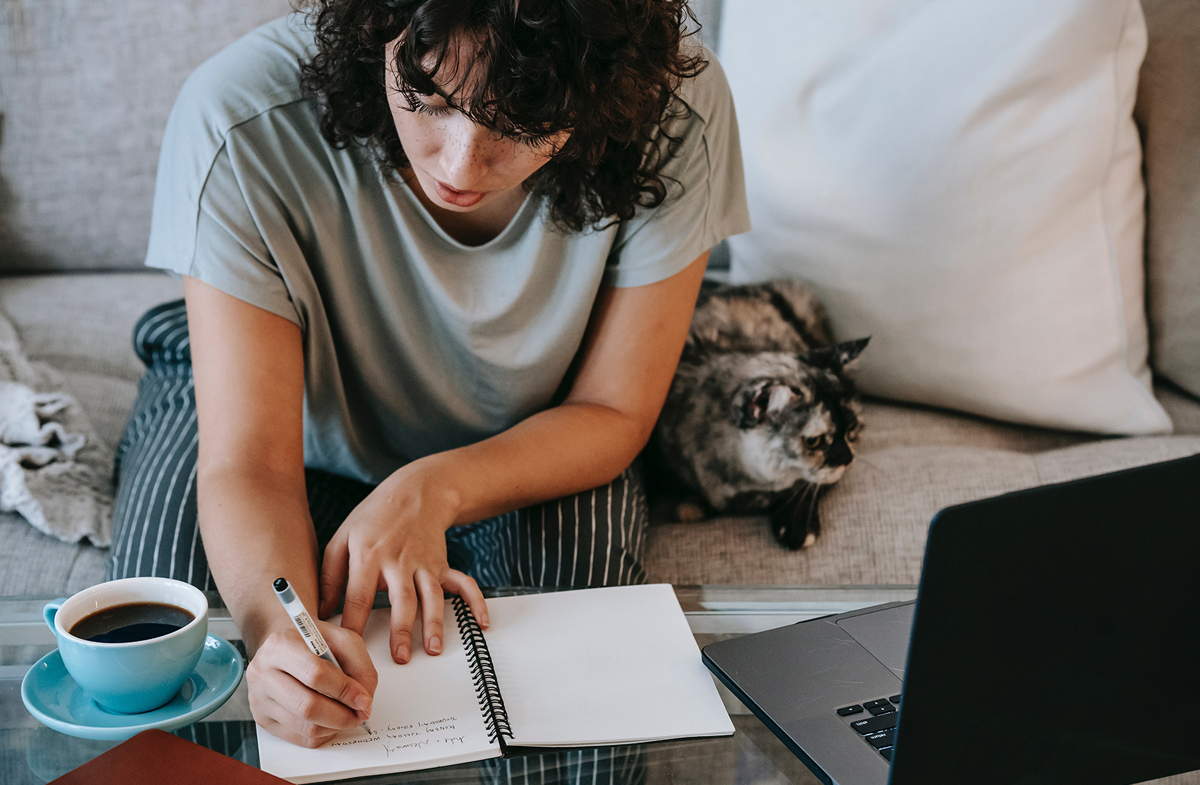 Woman writing in notebook at home with cat