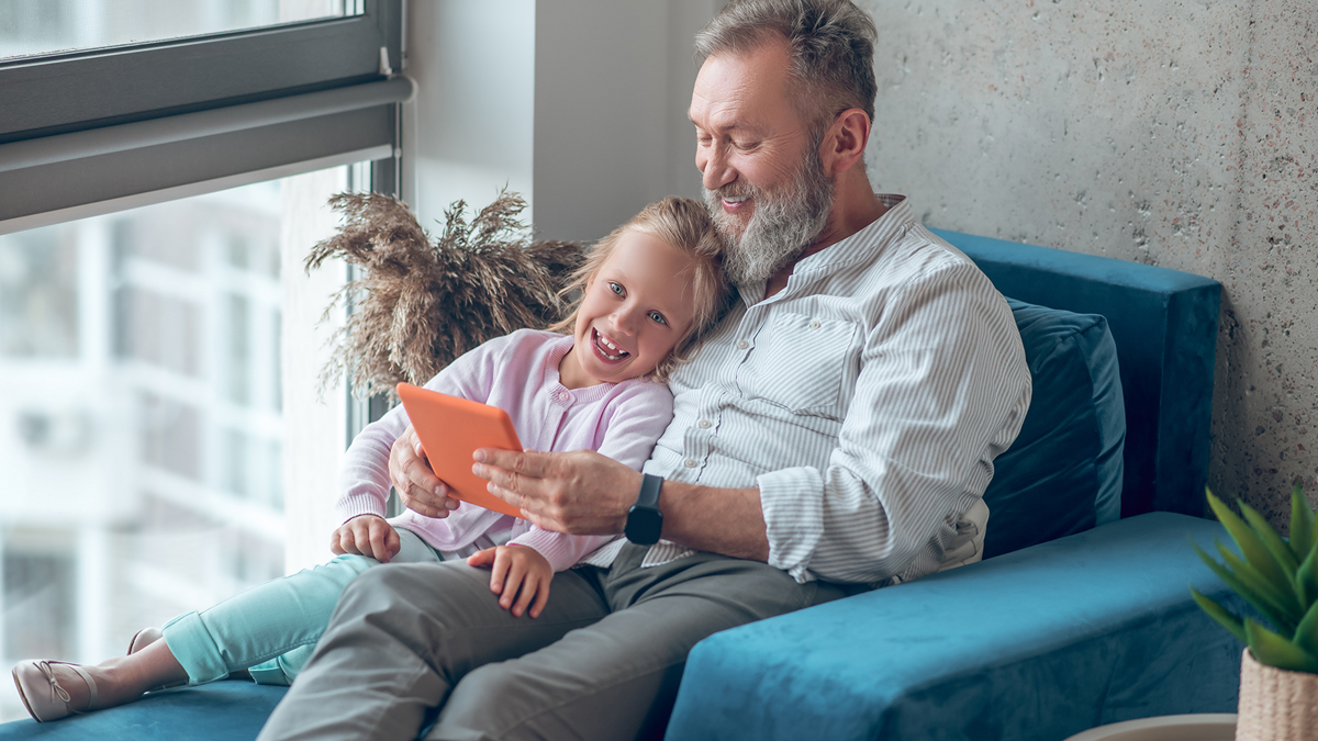 Little girl sitting with grandfather as they look at digital screen