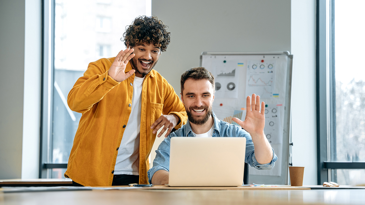 Two men waving at computer in an office