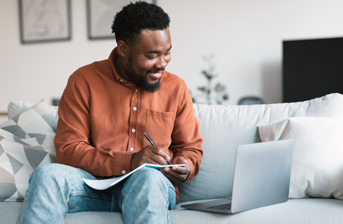 Adult man taking notes while learning on laptop