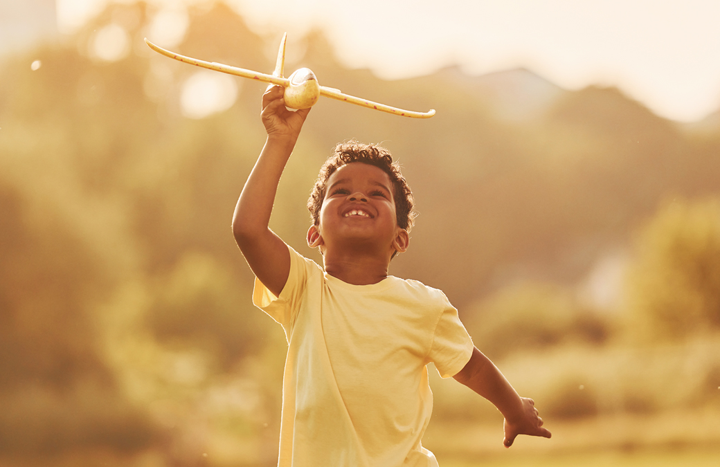 Little boy flying toy airplane in the summer sun