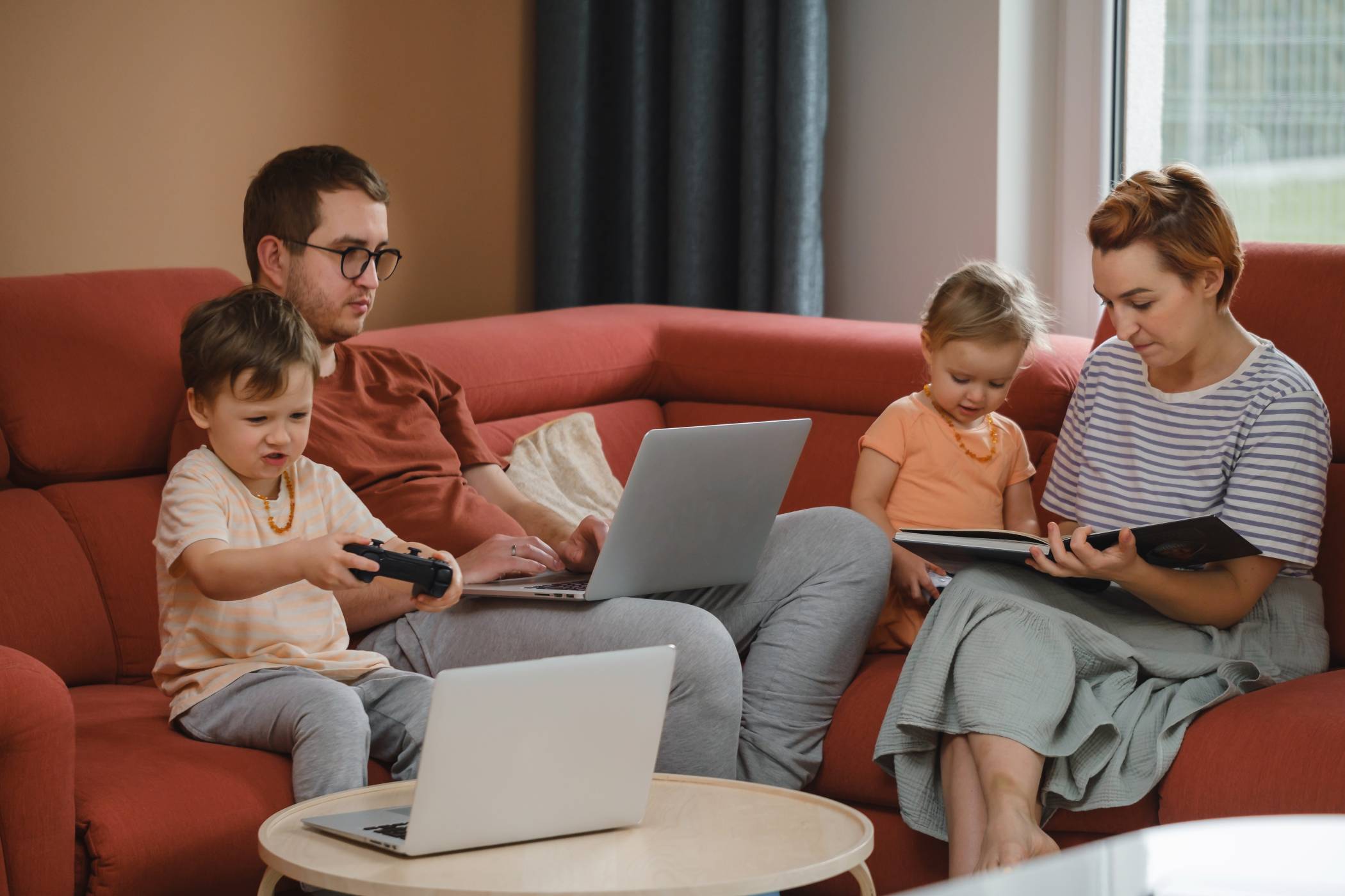 A family is gathered in the living room using various computers and electronic devices